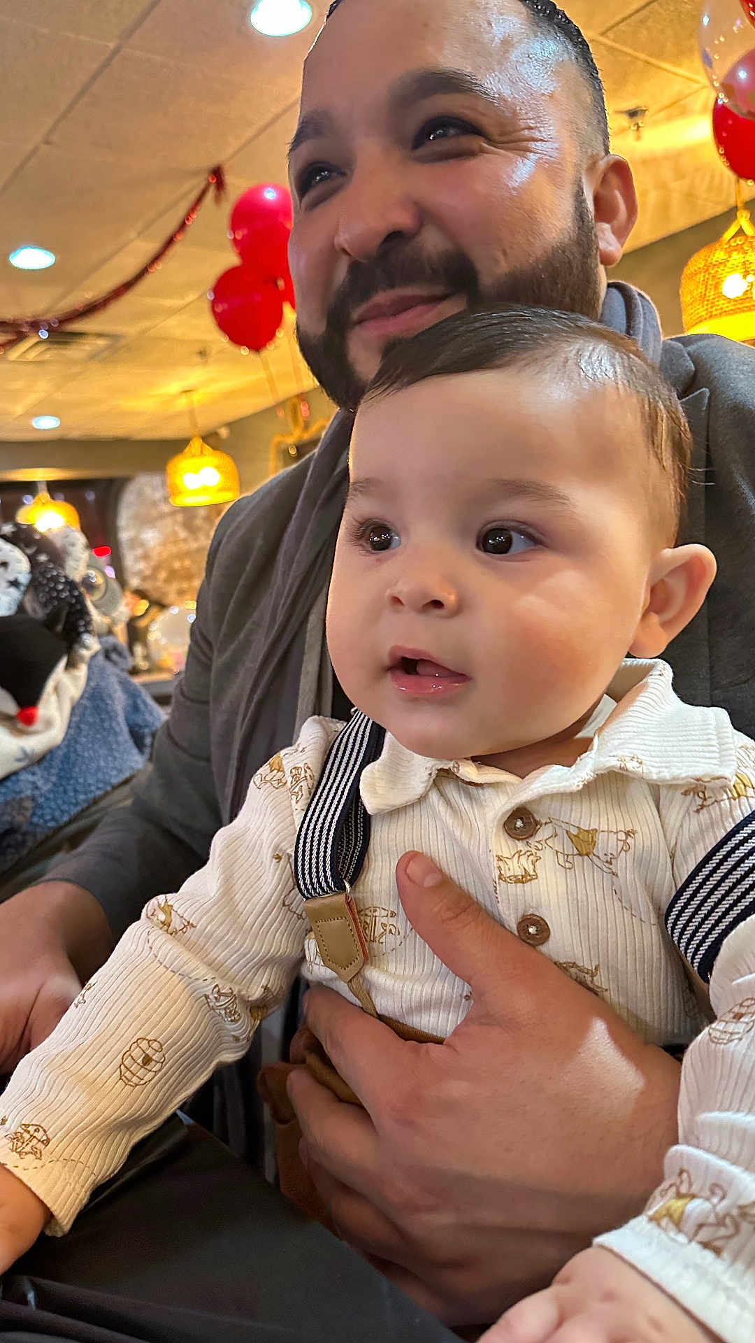 Emilio joined the competition — help win amazing prizes! baby, man, indoor, balloons, lighting, smile, face, hand, clothing, suspenders, beard, curious, warm_light, celebration, portrait, people, holding, event, table, background