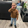 Emiliano is registered to the contest to win money with this photo: adult, box, boy, child, couch, family, furniture, hardwood_floor, indoor, jeans, living_room, peace_sign, person, plant, portrait, smile, sneakers, sweater, television, toddler