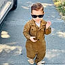 car, casual_clothing, child, cute, fashion, grass, hair, jumpsuit, outdoor, pavement, portrait, sandals, shadow, sidewalk, smile, street, sunglasses, sunny, toddler, walking