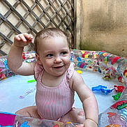 Léna a rejoint le concours — aidez-le/la à gagner de superbes lots ! arm, baby, child, colorful, cute, face, fun, happy, infant, inflatable_pool, outdoor, playful, sitting, skin, smiling, splashing, summer, swimsuit, water_toys, wooden_lattice