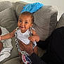 baby, child, smile, chain, necklace, couch, sofa, hand, clothing, white_shirt, blue_shirt, indoor, person, furniture, happy, infant, face, living_room, support, casual