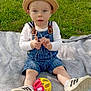 baby, child, hat, denim_overalls, toy, ball, blanket, grass, park, trees, sunlight, shoes, sitting, outdoor, nature, greenery, person, cute, infant, playful