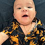 Julian Rodriguez is registered to the contest to win money with this photo: baby, child, smile, face, necklace, shirt, black, orange, patterned_clothing, open_mouth, lying_down, happy, cute, infant, person, portrait, jewelry, closeup, indoors, texture