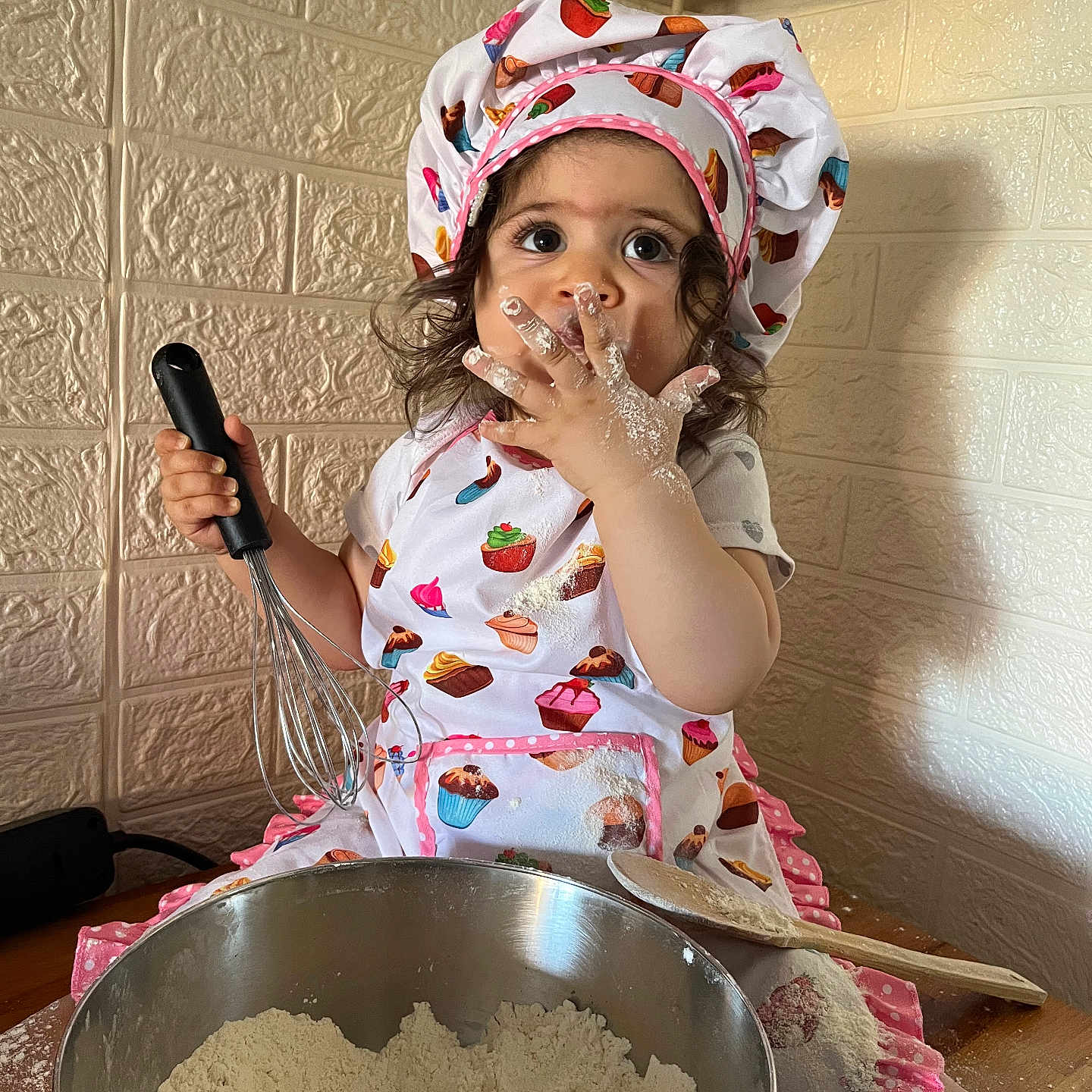Diora participe au concours pour gagner de l'argent avec cette photo : apron, baking, bowl, chef_hat, child, cooking, cute, face, flour, food, hands, indoors, kitchen, messy, person, playful, table, toddler, whisk, wooden_spoon