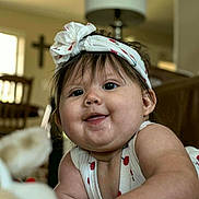 Addison is registered to the contest to win money with this photo: baby, child, smile, headband, indoor, furniture, living_room, cute, chubby_cheeks, person, happy, close_up, infant, playful, clothing, portrait, home, soft_lighting, young, face