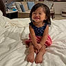 Raeyaa Jhade is registered to the contest to win money with this photo: toddler, child, smiling, bed, white_bedspread, dress, indoor, living_room, cushions, lamp, furniture, happy, sitting, person, portrait, cute, young_child, hair, feet, room