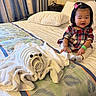 toddler, child, baby, bed, towel_art, plush, indoor, curtains, pillow, blanket, dress, hair_clip, wristband, smiling, furniture, person, portrait, room, decor, cute