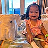 baby, toddler, child, indoor, bed, towel_animal, elephant, toy, pink_clothing, smile, person, curtains, window, bracelet, holding, relaxing, photography, happy, furniture, home