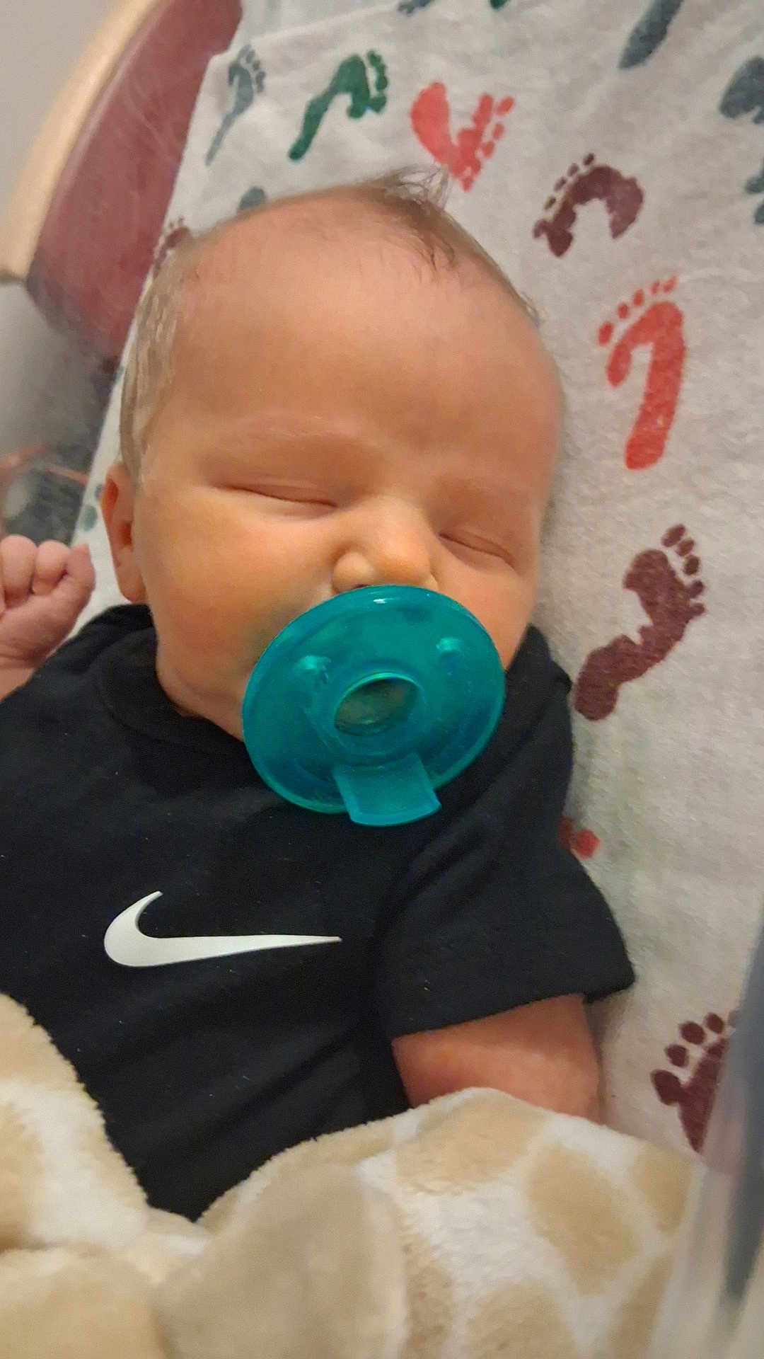 Axel is registered to the contest to win money with this photo: baby, pacifier, sleeping, blanket, footprint_pattern, onesie, black_clothing, infant, child, indoor, cute, peaceful, rest, soft_texture, head, face, small_hand, bed, fabric, comfort