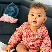 Jade participe au concours pour gagner de l'argent avec cette photo : baby, child, sitting, couch, clothing, pink_top, socks, book, curly_hair, face, hand, indoor, furniture, expression, skin, person, cute, messy_face, bright_eyes, casual