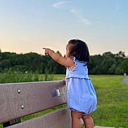 Alisa joined the competition — help win amazing prizes! toddler, child, bench, park, outdoor, grass, sky, greenery, romper, shoes, pointing, side_view, summer, nature, standing, cute, daylight, walking_path, casual, young_child