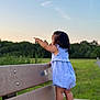 toddler, child, bench, park, outdoor, grass, sky, greenery, romper, shoes, pointing, side_view, summer, nature, standing, cute, daylight, walking_path, casual, young_child