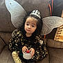 Scarlette is registered to the contest to win money with this photo: child, fairy_wings, tiara, dress, golden_leggings, tape_dispenser, couch, indoor, curly_hair, black_hair, decorative, seated, costume, young_child, playful, portrait, cute, fingertips, holding, expression