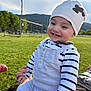 baby, child, smiling, outdoor, grass, field, hat, striped_clothing, person, happy, hands, nature, daylight, hill, casual_clothing, cute, infant, sitting, toothy_smile, playful