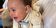 Aïden participe au concours pour gagner de l'argent avec cette photo : baby, child, infant, smiling, laughing, person, adult, clothing, vest, bow_tie, white_shirt, indoor, couch, furniture, people, family, happy, casual, seated, living_room