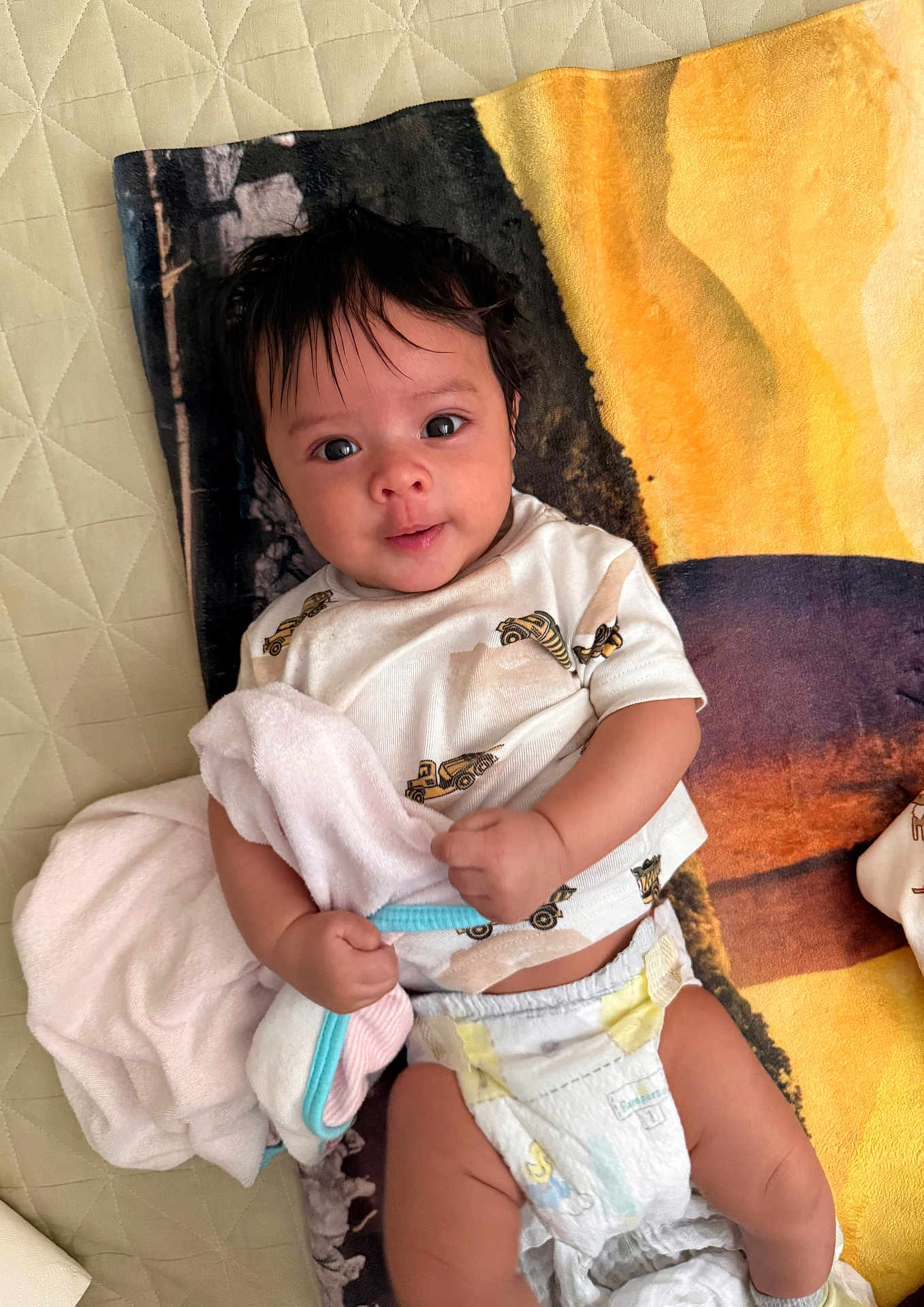 Arjun is registered to the contest to win money with this photo: baby, infant, towel, blanket, diaper, shirt, cute, lying_down, clothing, child, bed, soft, hand, face, smiling, indoors, person, young, comfort, playful