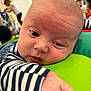 baby, infant, close_up, face, hand, striped_clothing, green_cushion, indoor, child, person, curious, resting, soft_light, background_blur, people, casual, expression, young_child, early_childhood, candid