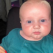 Tommy is registered to the contest to win money with this photo: baby, infant, child, face, blue_eyes, teal_clothing, animal_print, hand, red_nails, indoor, portrait, cute, closeup, person, skin, young, expression, holding, sitting, soft_light