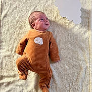 Leo participe au concours pour gagner de l'argent avec cette photo : baby, infant, onesie, orange_clothing, sheep_patch, blanket, soft_texture, lying_down, curious_expression, indoors, newborn, cute, small_hands, small_feet, sleepwear, child, portrait, face, head, skin