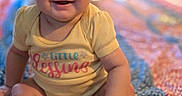 Raquel is registered to the contest to win money with this photo: baby, smiling, sitting, yellow_onesie, quilt, colorful, infant, happy, child, portrait, indoors, face, cute, feet, hands, young, clothing, expression, person, warm