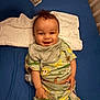 Ronan is registered to the contest to win money with this photo: baby, smiling, pajamas, animal_print, infant, child, bed, blue_bedspread, blanket, happy, cute, clothing, person, lying_down, indoors, head, face, hand, toddler, soft_fabric