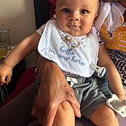 Ronan is registered to the contest to win money with this photo: baby, child, bib, indoor, person, hand, clothing, pacifier, shorts, sitting, skin, face, cute, holding, expression, newborn, family, comfort, adult, casual