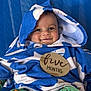 Ronan is registered to the contest to win money with this photo: baby, child, smiling, towel, blue, white, hood, sign, wooden_sign, five_months, colorful_pants, patterned_clothing, sitting, portrait, indoor, close_up, cute, happy, infant, face