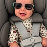 baby, child, infant, smiling, sunglasses, red_bow, car_seat, safety_harness, portrait, close_up, happy, indoors, seated, patterned_clothing, hello_kitty, gray_background, face, fashion, cute, photography