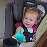 toddler, car_seat, child, toy, blue, car_interior, seatbelt, smiling, hair, pony_tail, window, daylight, backseat, human, person, clothing, seat, safety, happy, automobile
