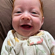 Emery is registered to the contest to win money with this photo: baby, red_hair, smiling, onesie, cozy, infant, face, happy, cute, child, portrait, soft, cushion, clothing, closeup, resting, indoor, young, skin, expression