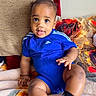baby, infant, child, blue_clothing, onesie, socks, sitting, blanket, pillow, floral_pattern, indoor, cute, face, portrait, smiling, looking_at_camera, skin, hands, legs, comfortable