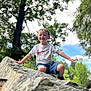 child, boy, smiling, outdoor, rock, tree, nature, sky, greenery, tshirt, shorts, playful, happy, daylight, casual_clothing, person, portrait, fun, balance, summer