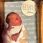 Elyas is registered to the contest to win money with this photo: newborn, baby, blanket, swaddled, hospital, bassinet, infant, bed, sleeping, clothing, person, face, hand, cute, lying_down, soft, cozy, wrapped, baby_bed, newborn_baby
