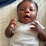 Linda Marie joined the competition — help win amazing prizes! baby, infant, child, onesie, bed, blanket, striped_sheet, hand, face, cute, lying_down, indoors, expression, newborn, skin, curly_hair, person, young, sleepwear, soft