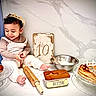 child, toddler, crown, rolling_pin, pastries, butter, baking, sign, table, smile, happy, kitchen, plate, flour, bowl, cooking, celebration, food, sitting, portrait