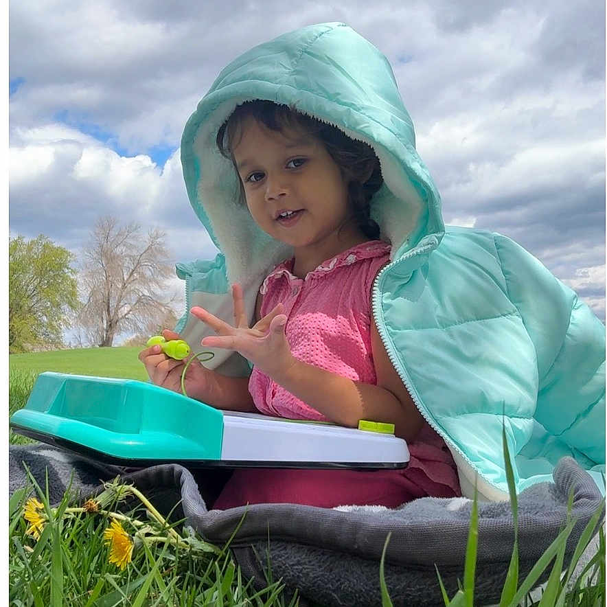 Sriaadhya is registered to the contest to win money with this photo: blanket, casual_clothing, child, cloudy_sky, curious, dandelions, daytime, grass, greenery, hood, jacket, nature, outdoor, person, play, portrait, sitting, smiling, toy, young_child