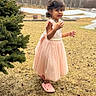 background, casual_footwear, child, curly_hair, daylight, dress, earrings, expression, girl, grass, nature, outdoor, person, pine_tree, pink_crocs, portrait, seasonal, standing, winter, young