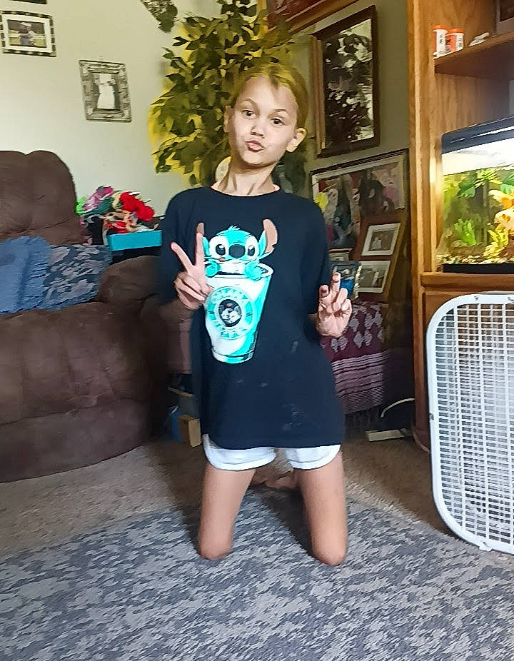 Lilyann is registered to the contest to win money with this photo: brown_hair, couch, electric_blue, flooring, fun, hairstyle, human_leg, knee, neck, pattern, person, picture_frame, room, shorts, sitting, sleeve, sportswear, t_shirt, thigh, toddler