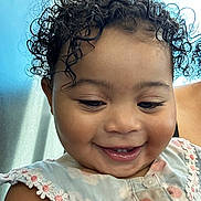 Patience is registered to the contest to win money with this photo: toddler, child, smiling, curly_hair, dress, floral, close_up, portrait, happy, cute, baby, face, skin, eyelashes, indoors, person, joyful, natural_light, clothing, daisy