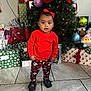 child, toddler, christmas_tree, presents, holiday, red_sweater, patterned_pants, shoes, floor_tiles, indoor, decorations, gift_wrap, bow, holiday_lights, festive, cute, smiling, celebration, home, portrait