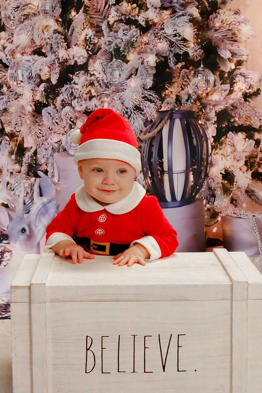 Aubrey is registered to the contest to win money with this photo: baby, baby_toddler_clothing, cap, child, christmas, christmas_eve, event, happy, head, headwear, holiday, joy, person, pink, plant, red, smile, standing, toddler, tree