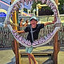 child, boy, shark_jaw, amusement_park, sign, le_splash, cap, black_tshirt, shorts, smiling, playful, daylight, outdoor, bench, wooden_frame, rides, people, fence, fun, summer