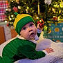 baby, bells, blanket, child, christmas, cute, decorations, elf_costume, festive, green_clothing, hat, holiday, holiday_season, indoor, lights, portrait, presents, smiling, toddler, tree