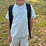 Bryson is registered to the contest to win money with this photo: child, boy, smile, backpack, shorts, shirt, outdoor, grass, sunlight, yard, fence, happy, casual_clothing, shoes, black_socks, summer, nature, young, portrait, standing