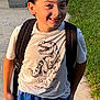Bryson is registered to the contest to win money with this photo: child, boy, smile, outdoor, tshirt, dinosaur, shorts, backpack, grass, plants, concrete, sunlight, happy, casual, portrait, person, young, nature, greenery, summer