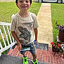 boy, child, smiling, dinosaur_tshirt, shorts, neon_sneakers, smartphone, porch, steps, grass, car, driveway, trees, outdoor, happy, casual_clothing, playing, summer, front_yard, daylight