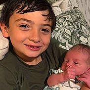 Bryson is registered to the contest to win money with this photo: child, baby, smiling, holding, blanket, bedroom, pillow, newborn, face, person, indoors, happy, sibling, family, portrait, young_child, toddler, clothing, resting, closeup