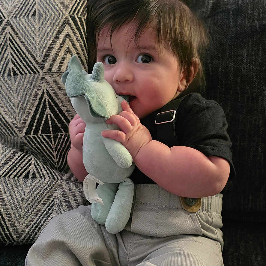 Cristian joined the competition — help win amazing prizes! baby, barefoot, child, clothing, couch, curly_hair, cute, face, geometric_pattern, hand, home, indoor, infant, pants, pillow, plush_toy, shirt, sitting, stuffed_animal, toys