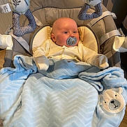 Luca is registered to the contest to win money with this photo: baby, baby_seat, blanket, blue, child, clothing, comfort, cushion, cute, expression, face, flooring, head, indoor, infant, pacifier, plush, soft_toy, toy, warm