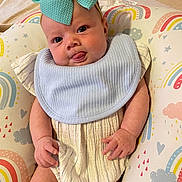 Laylah joined the competition — help win amazing prizes! baby, infant, bow, blue_bow, tongue_out, cute, smiling, face, hands, striped_outfit, bib, cushion, rainbow_pattern, colorful, soft_texture, indoors, child, playful, portrait, closeup